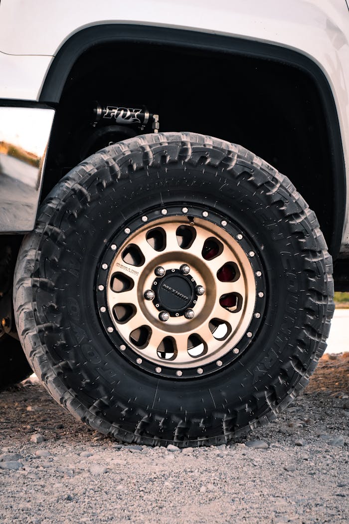 Detailed view of an off-road tire with rugged tread on a vehicle parked on gravel.